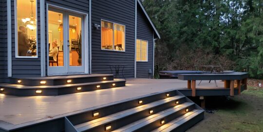 A deck with lighting and steps leading to a house.