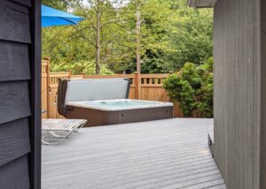 A backyard deck with a hot tub and a blue umbrella.