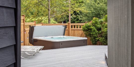 A backyard deck with a hot tub and a blue umbrella.